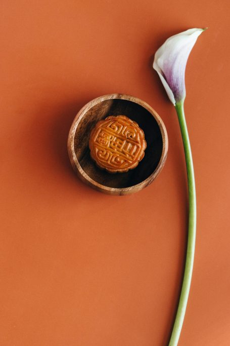 A spherical dessert in a small bowl next to a single white flower on an orange background.