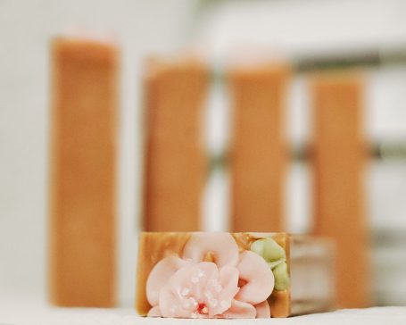 Close-up of a soap bar with a pink floral design, blurred background of stacked soap bars.