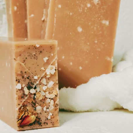 Natural soap bars with rose petals and oats, displayed on a soft white towel.